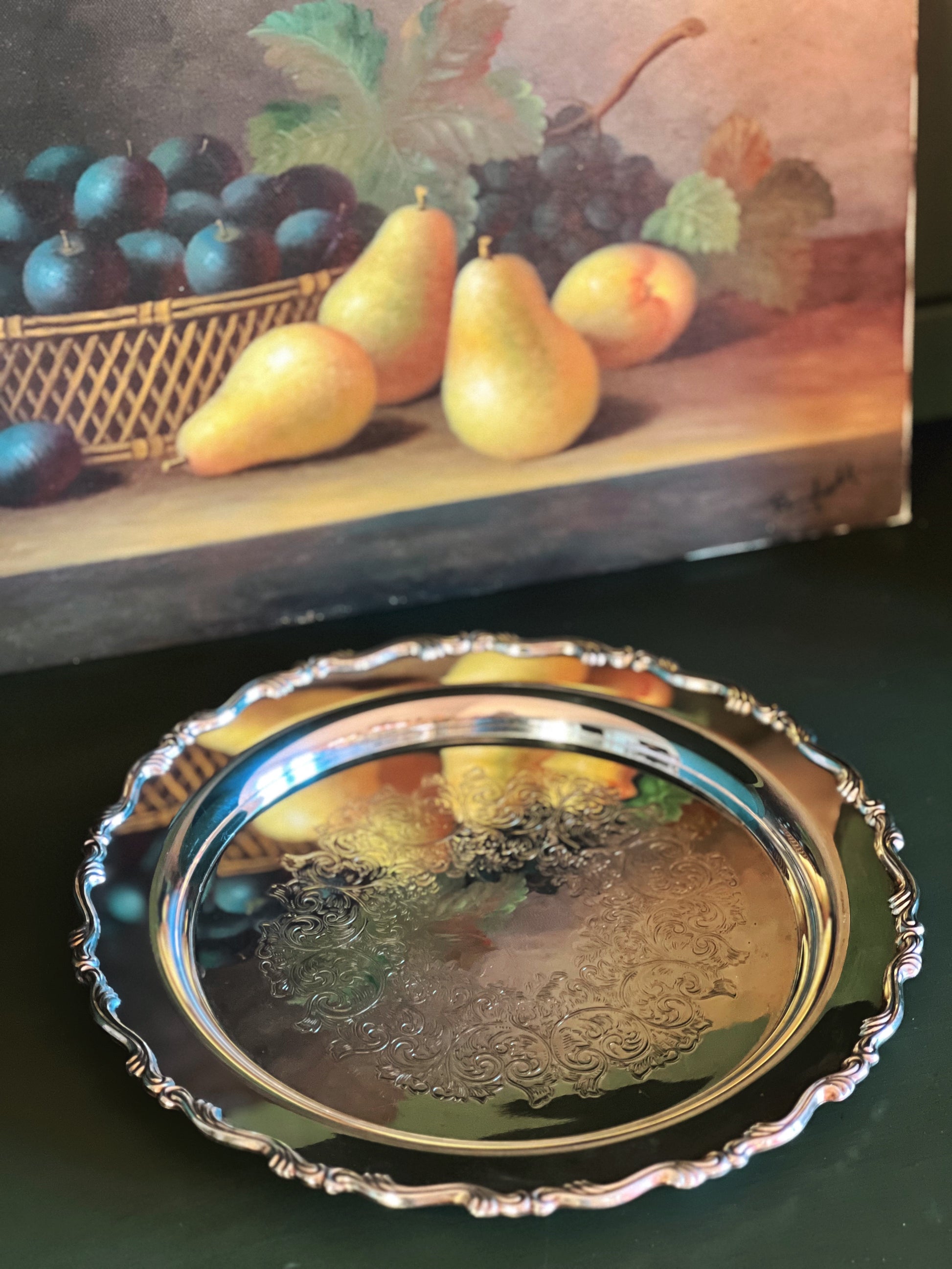 Decorative silver platter with fruit painting in the background