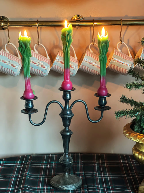 Decorative candelabra with lit candles in front of a row of mugs on a wall.