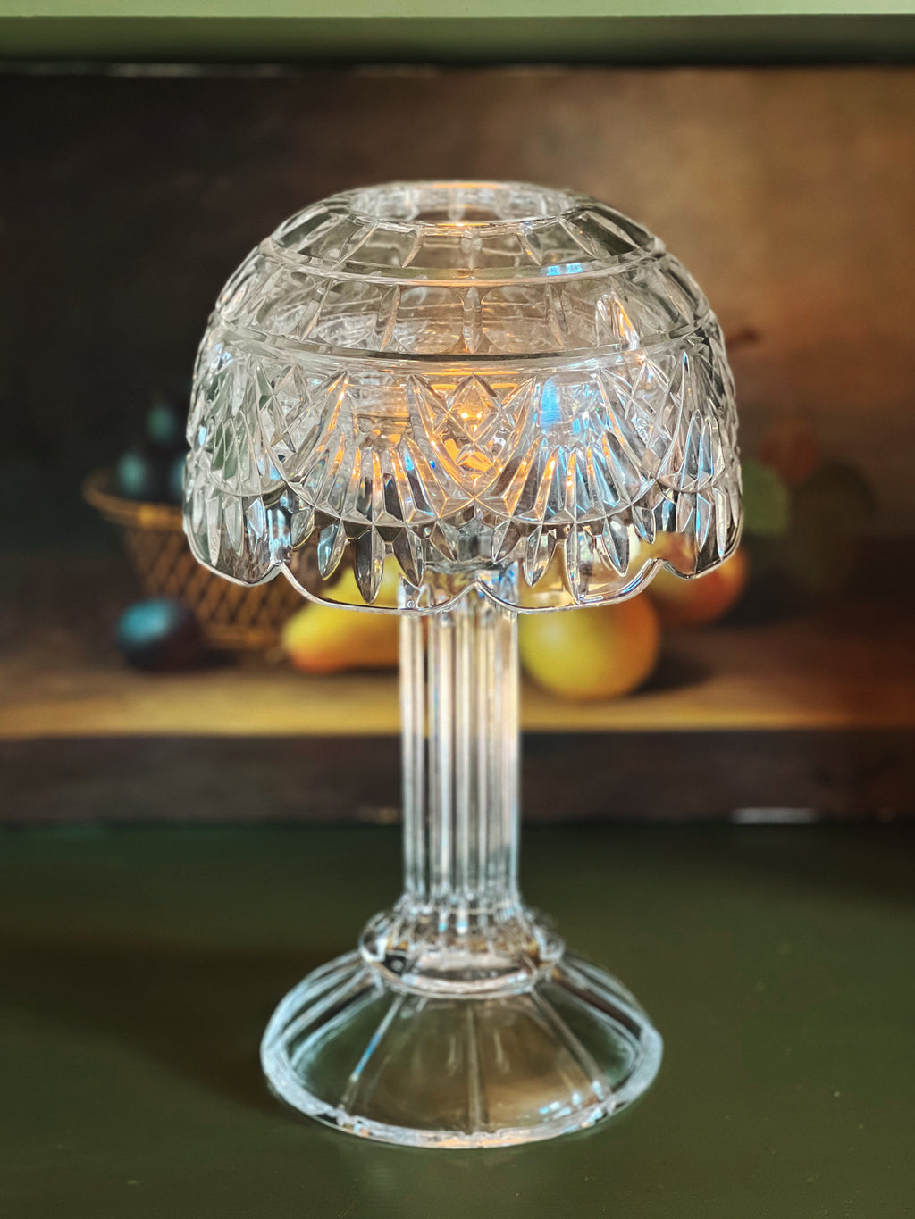 Clear glass candle holder on a wooden surface with fruits in the background