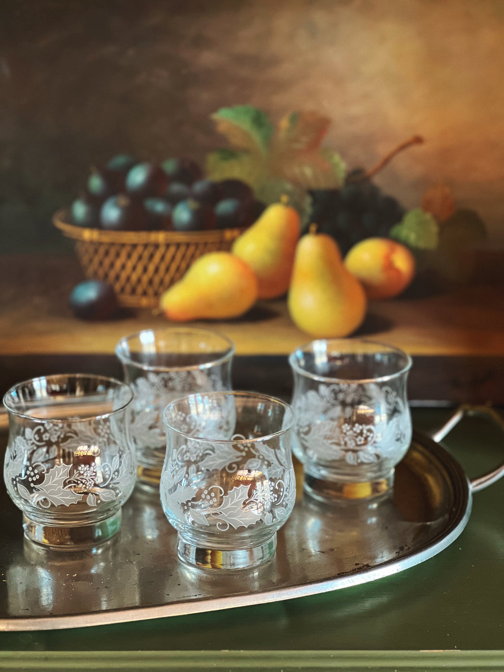 Set of four etched glass candle holders on a tray with fruits in the background