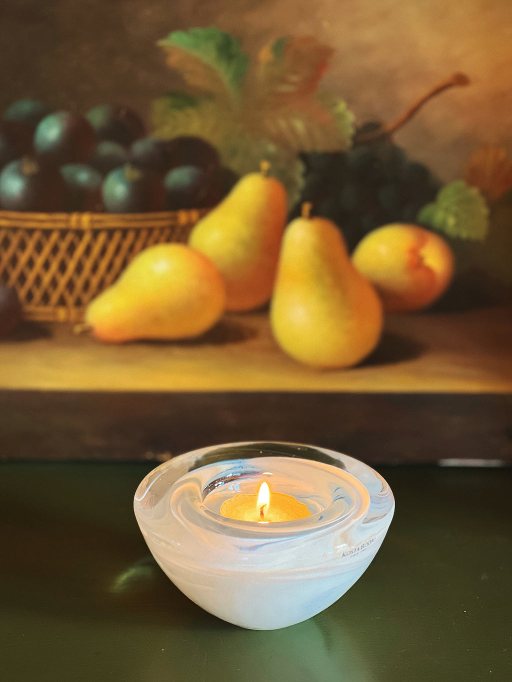 Tea light candle in a glass holder with pears and plums in the background