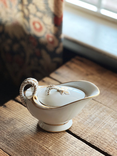 White ceramic gravy boat with gold accents on a wooden surface