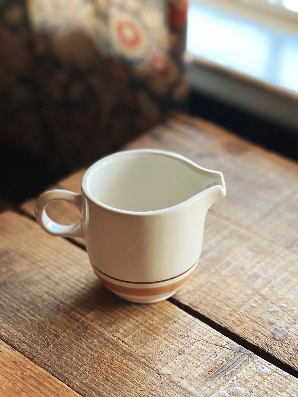 White ceramic pitcher with brown stripe on a wooden surface