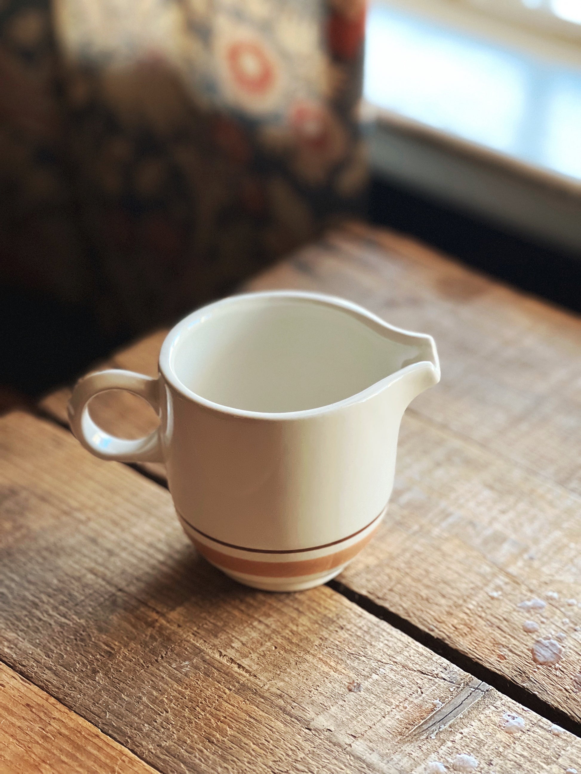White ceramic pitcher with brown stripe on a wooden surface