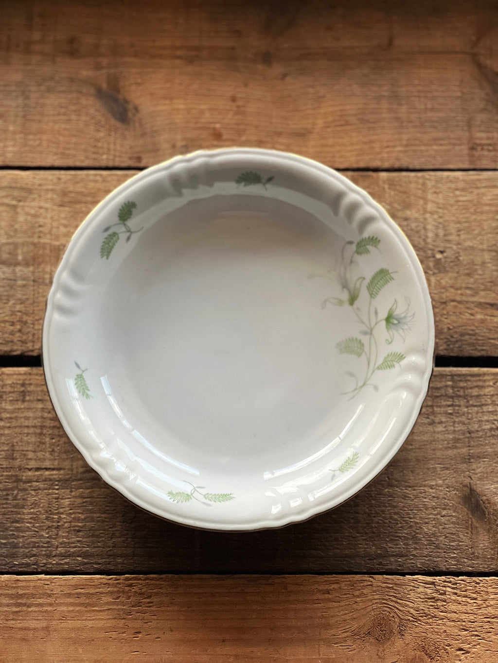 White ceramic pie dish with green floral patterns on a wooden surface