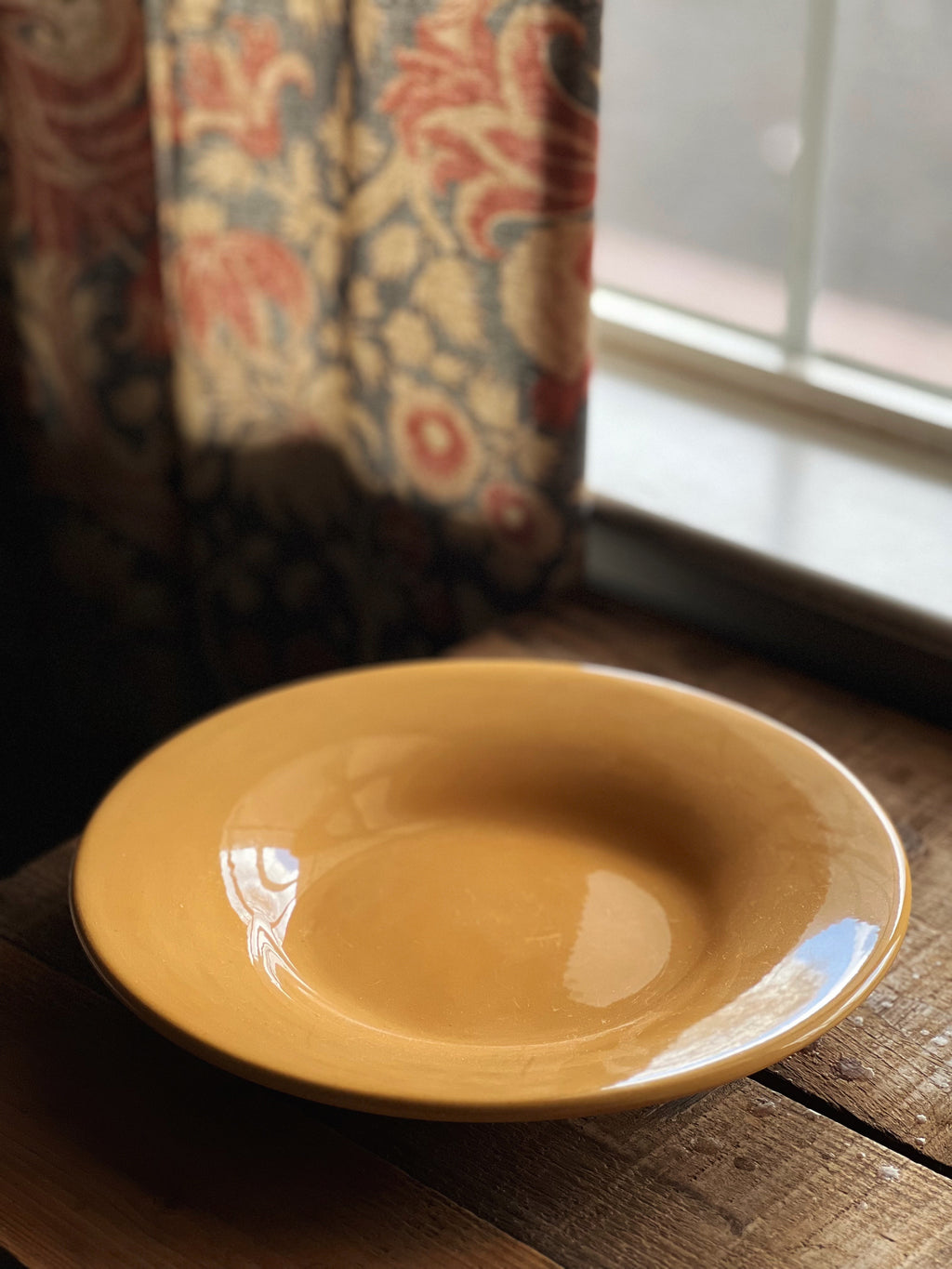 Yellow ceramic plate on a wooden surface with a patterned curtain in the background