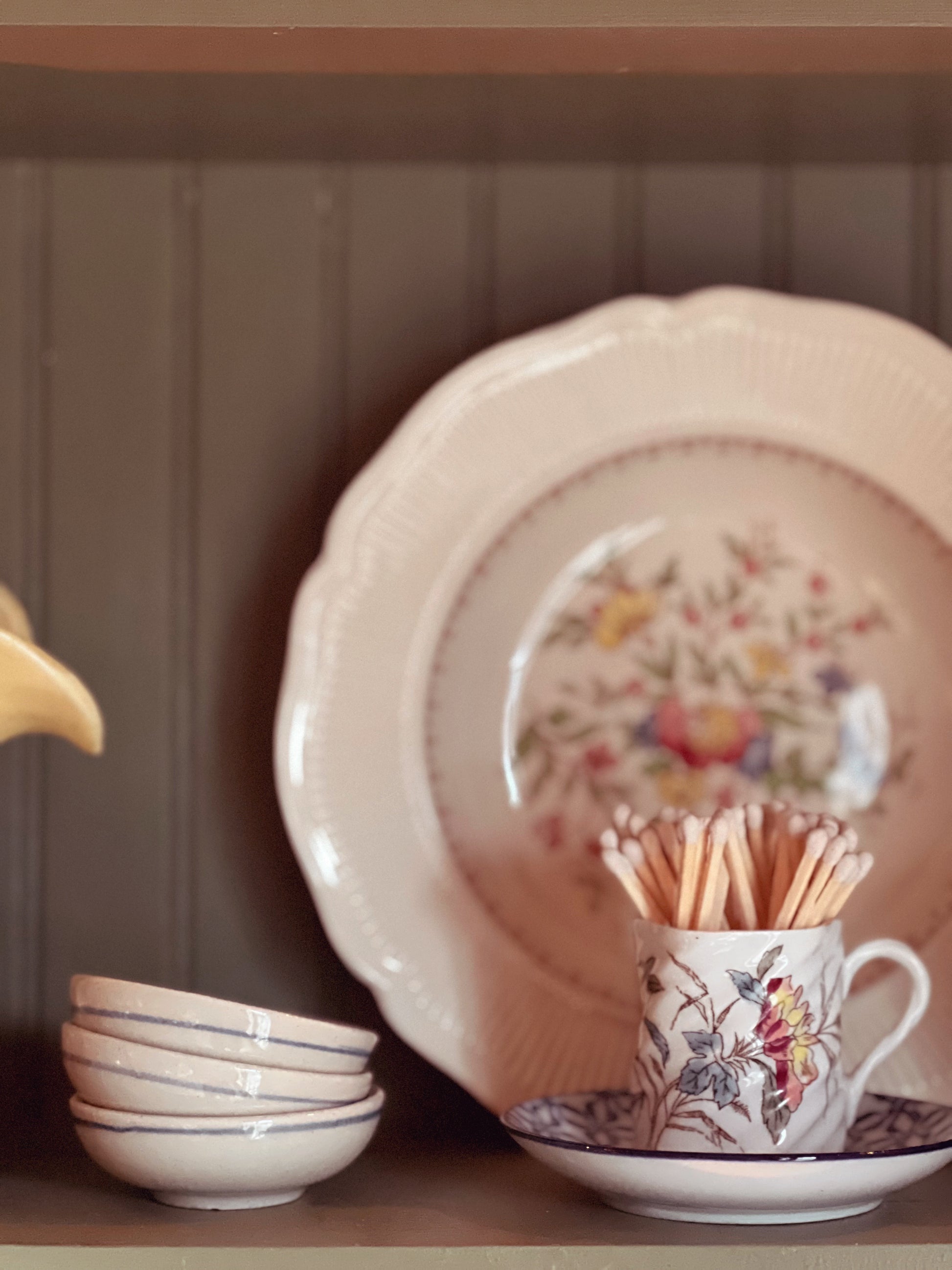 Decorative ceramic items including a teapot, plates, and cups with floral patterns on a wooden shelf.