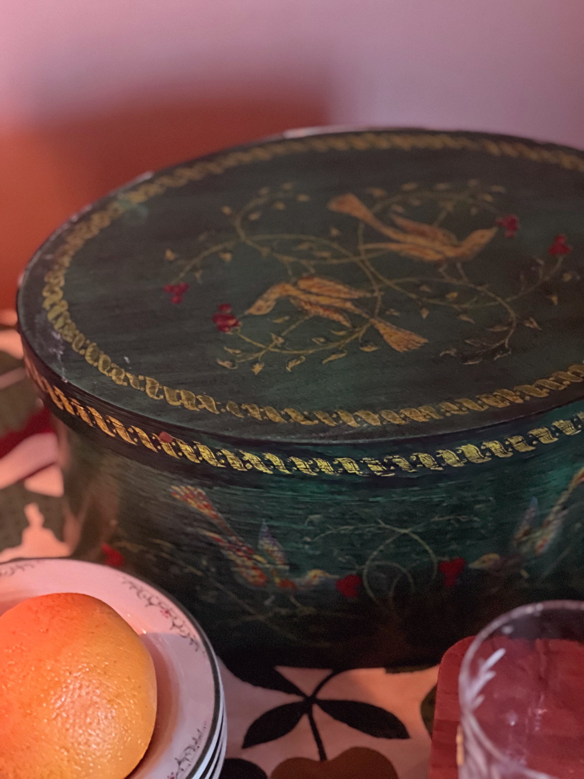Decorative round box with intricate designs on a table with an orange and glass.