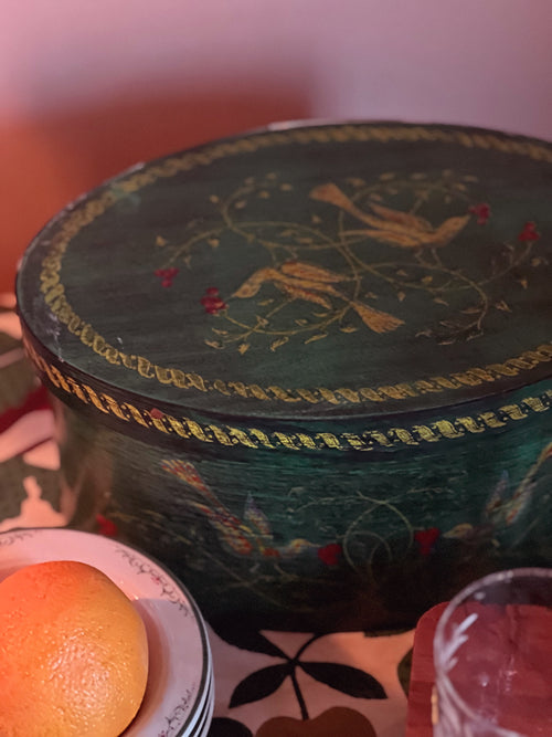 Decorative round box with intricate designs on a table with an orange and glass.