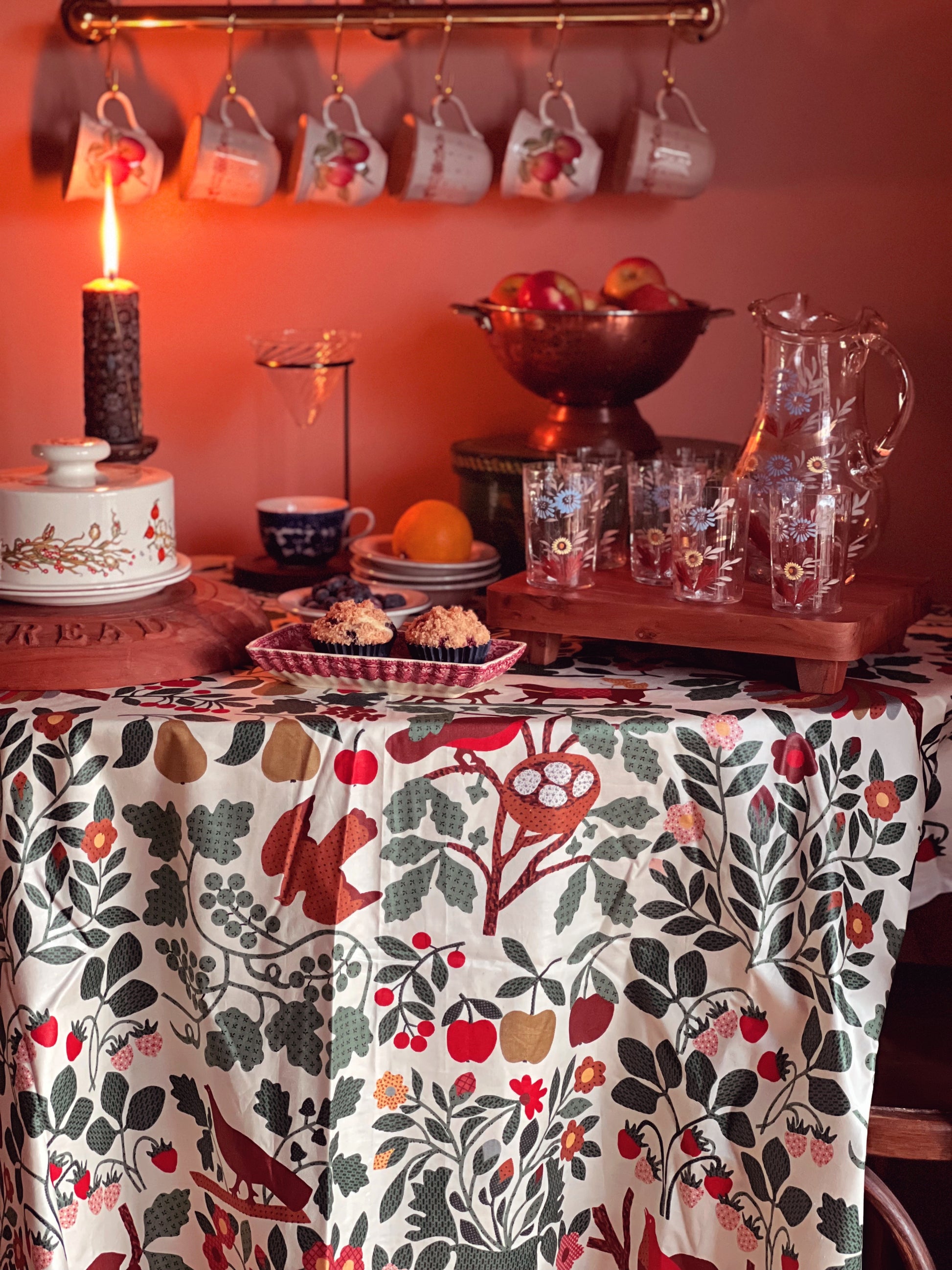Dining table with a floral tablecloth, fruit bowl, and decorative items.