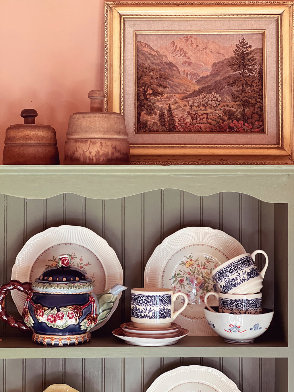 Decorative shelf with ceramic dishes and a framed landscape painting on a wall.