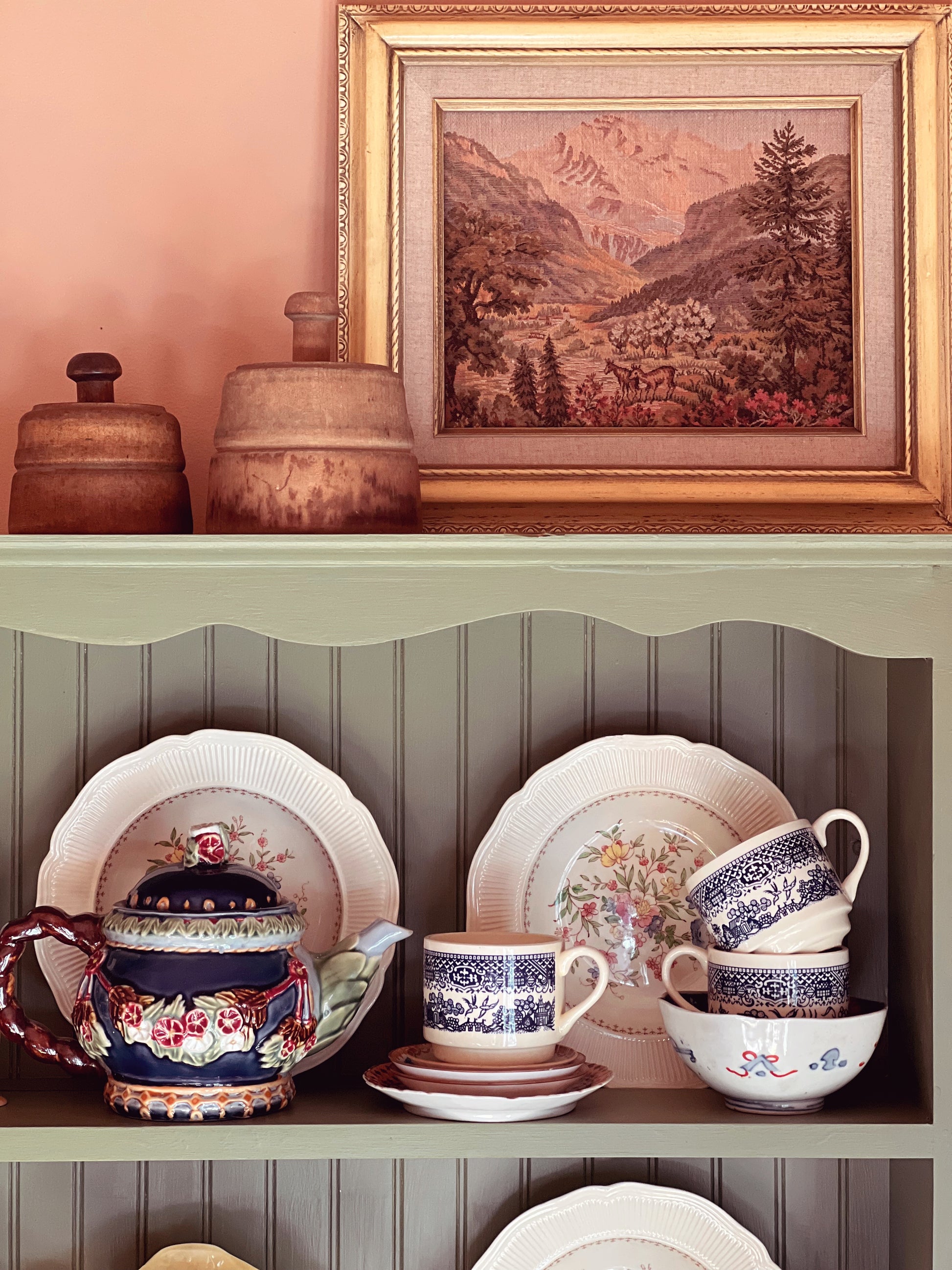 Decorative shelf with ceramic dishes and a framed landscape painting on a wall.