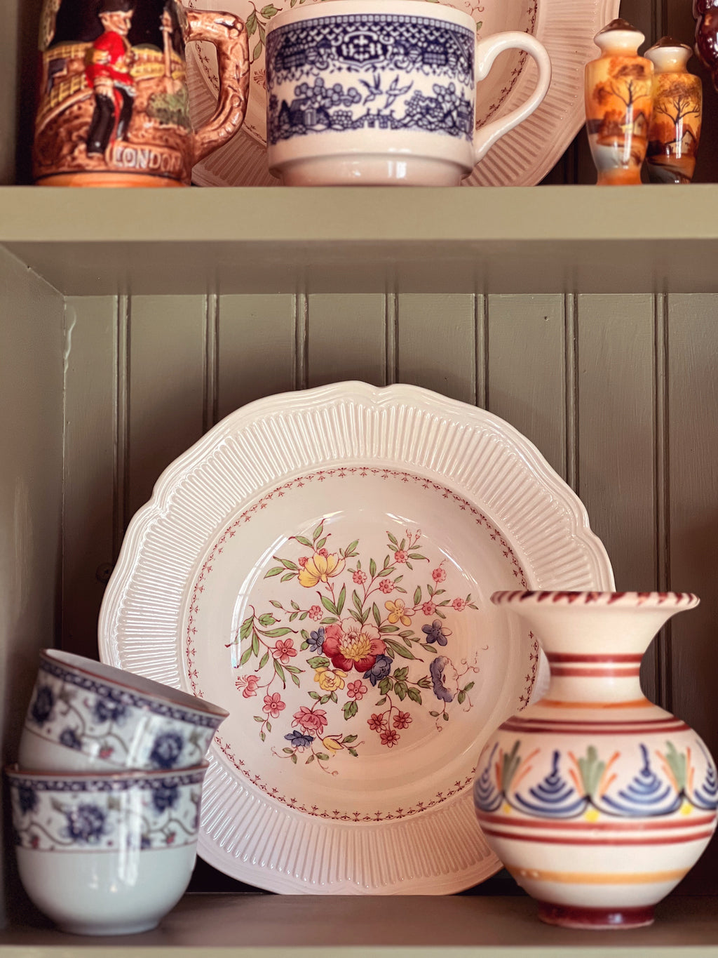 Ceramic plates with floral design and decorative vases on a shelf.