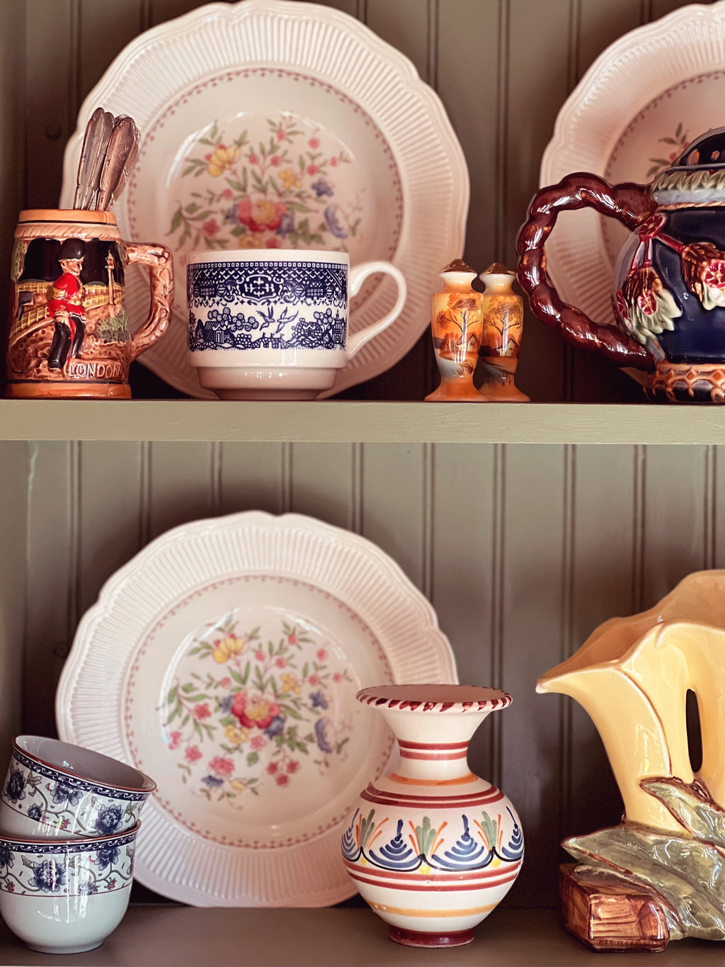 Collection of ceramic plates, mugs, and vases with floral patterns on a wooden shelf.