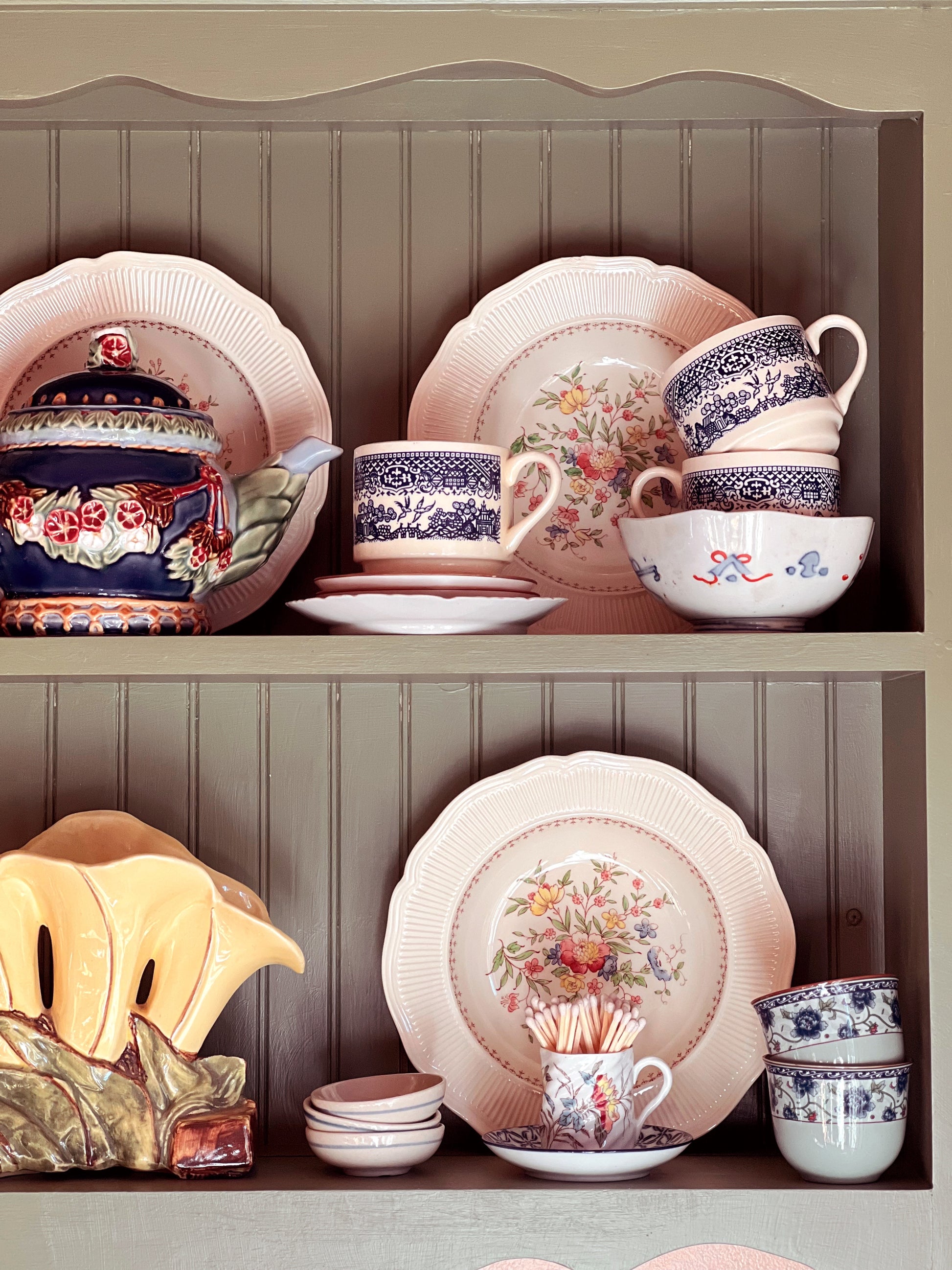 Collection of ceramic dishes and teapots on a wooden shelf against a beige wall.