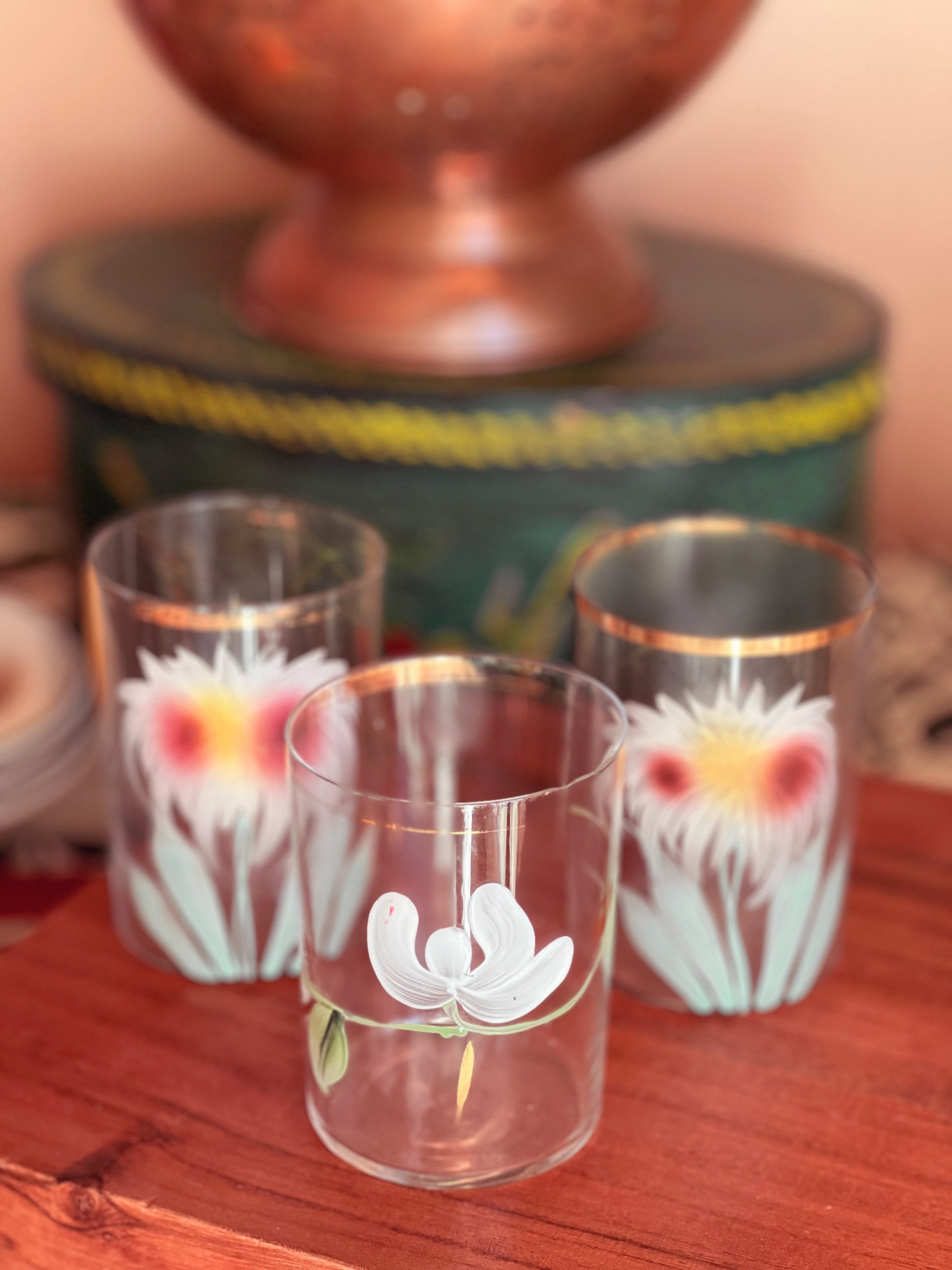 Three glass tumblers with floral designs on a wooden surface.