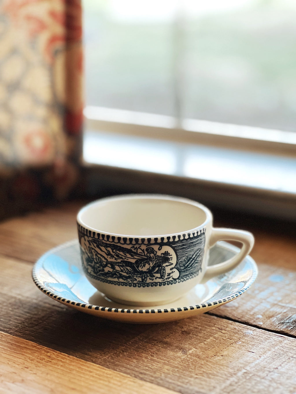 Ceramic cup and saucer with blue patterns on a wooden surface near a window.