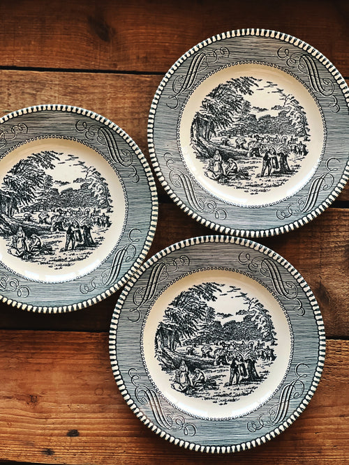 Three decorative plates with black and white scenes on a wooden surface