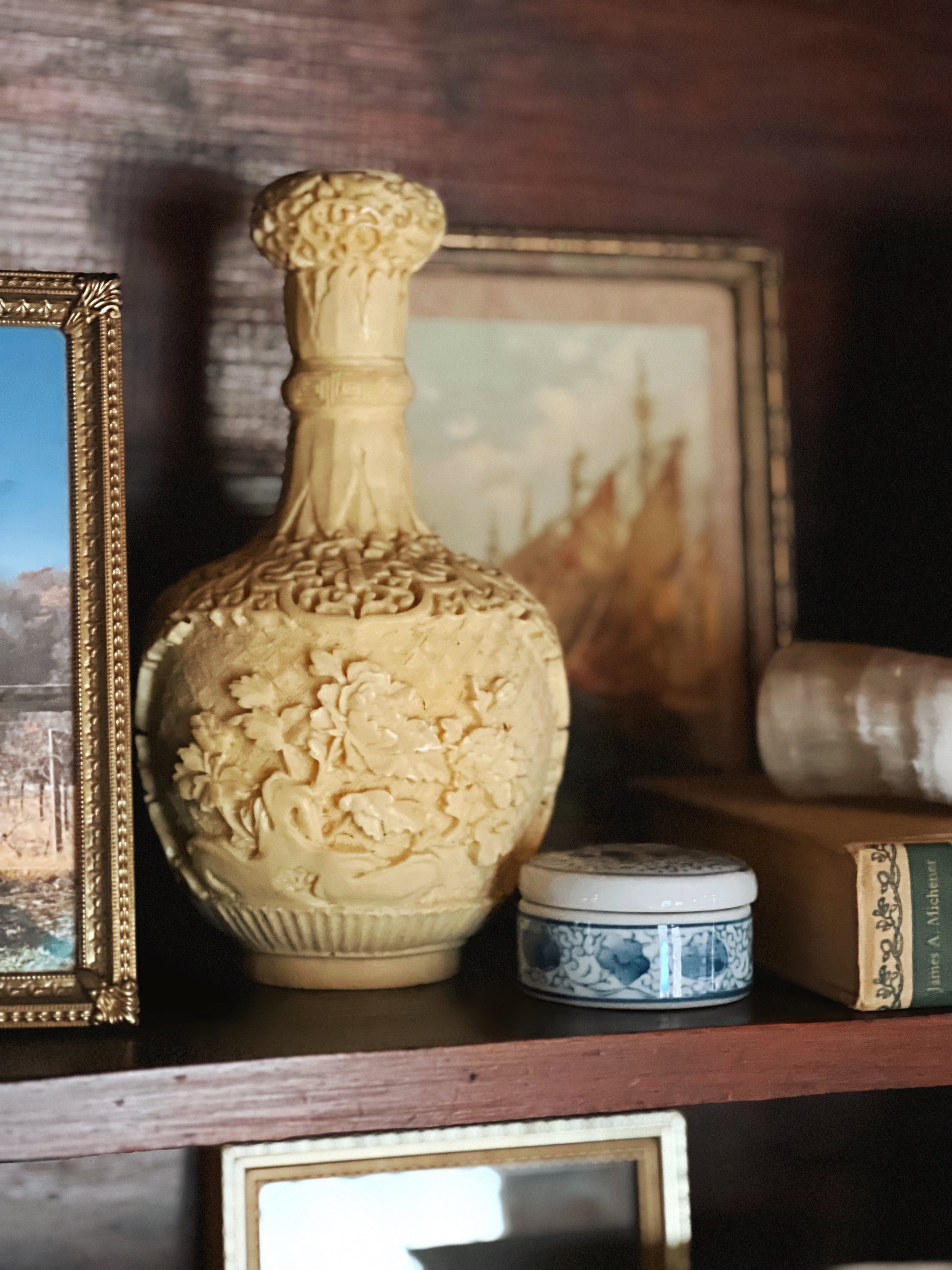 Decorative ceramic vase on a shelf with framed pictures and books in the background
