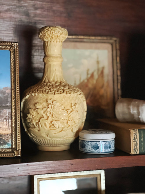 Decorative ceramic vase on a shelf with framed pictures and books in the background