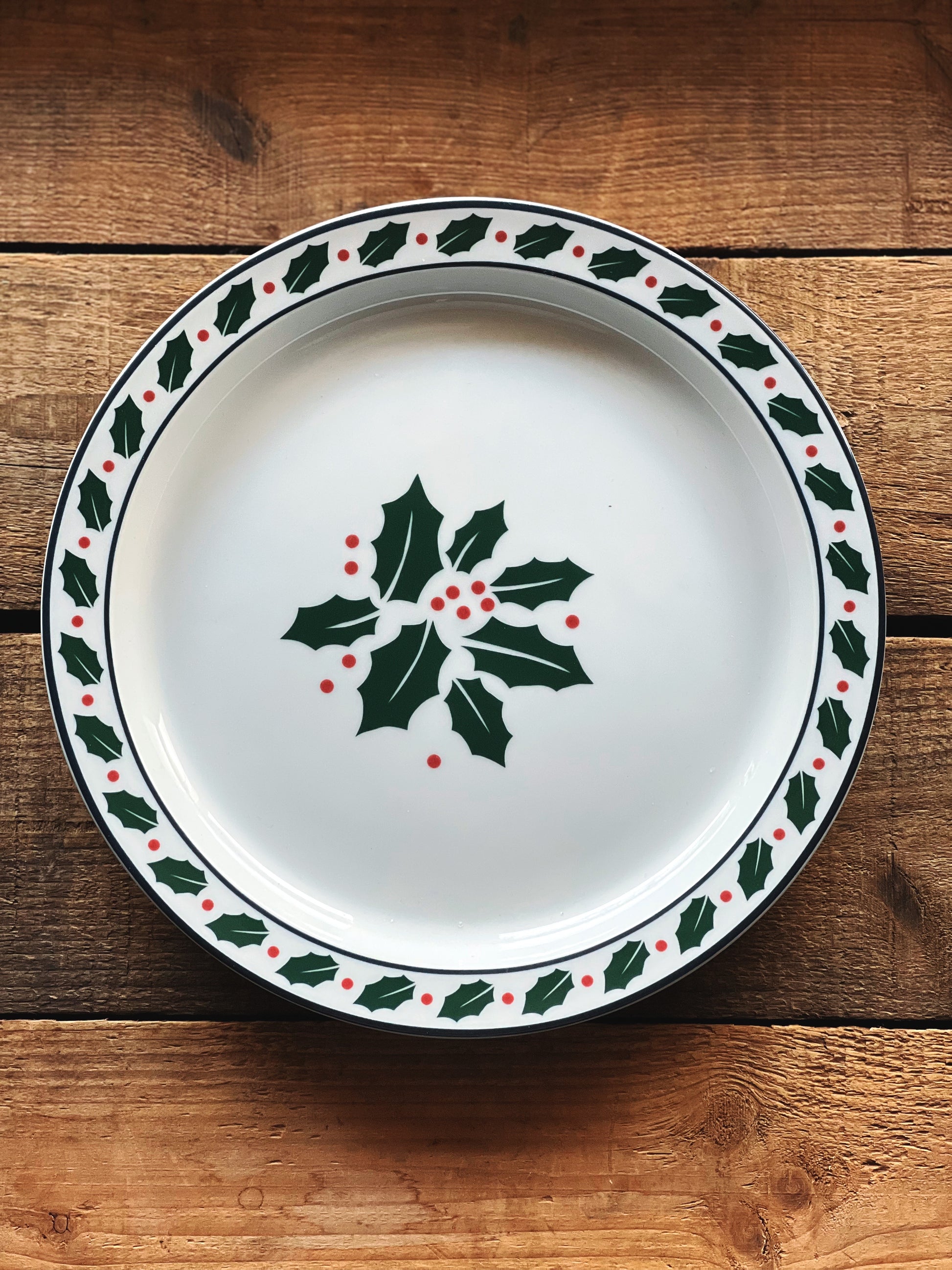 Decorative plate with holly design on a wooden surface