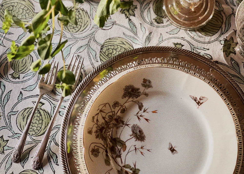 Decorative table setting with floral arrangement, plates, and cutlery on a patterned tablecloth.