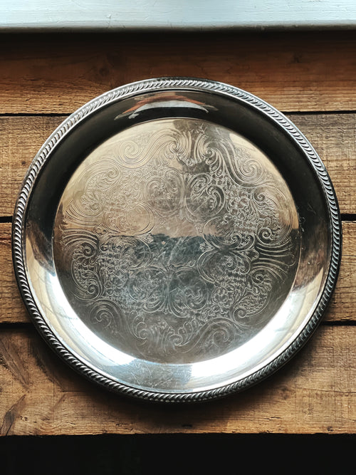 Silver decorative tray with intricate patterns on a wooden surface