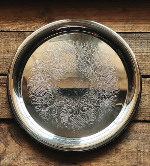 Decorative silver tray with intricate patterns on a wooden surface