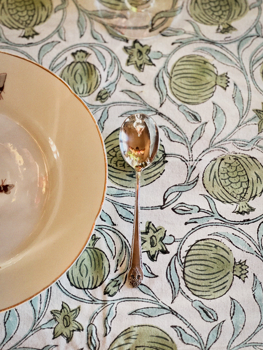 Table setting with a decorative tablecloth featuring green fruit patterns, a plate, and a spoon.