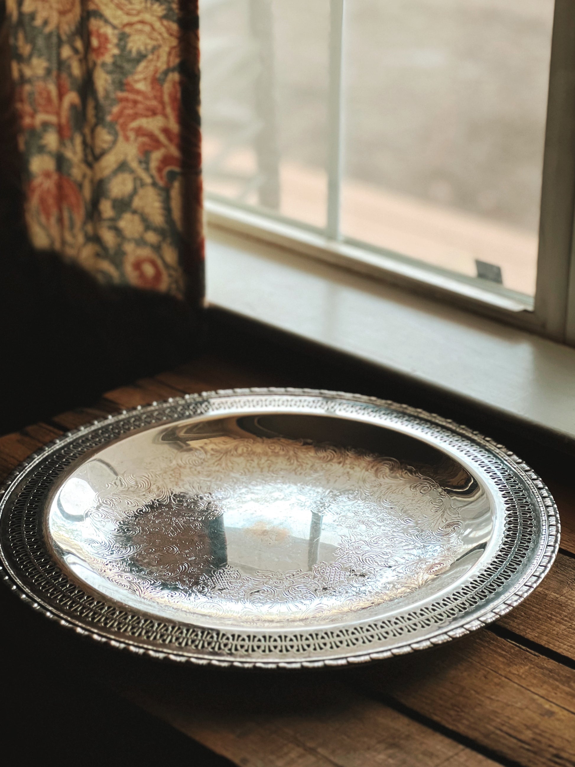 Silver decorative tray on a wooden surface with a window in the background