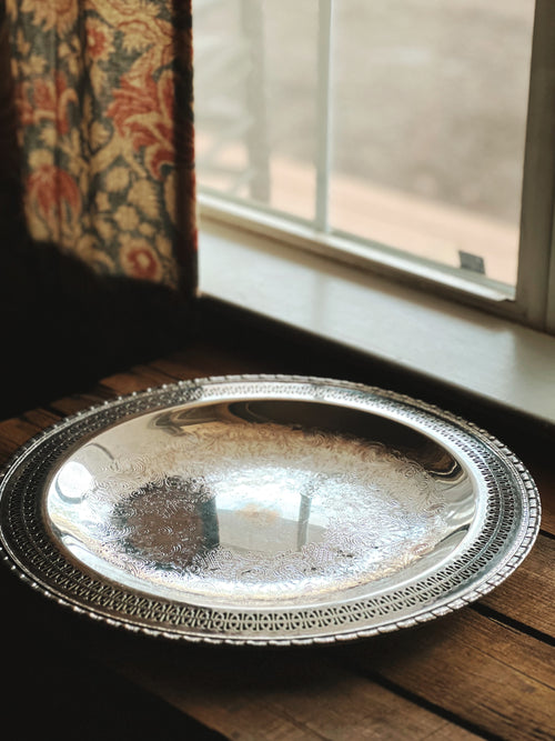 Silver decorative tray on a wooden surface with a window in the background