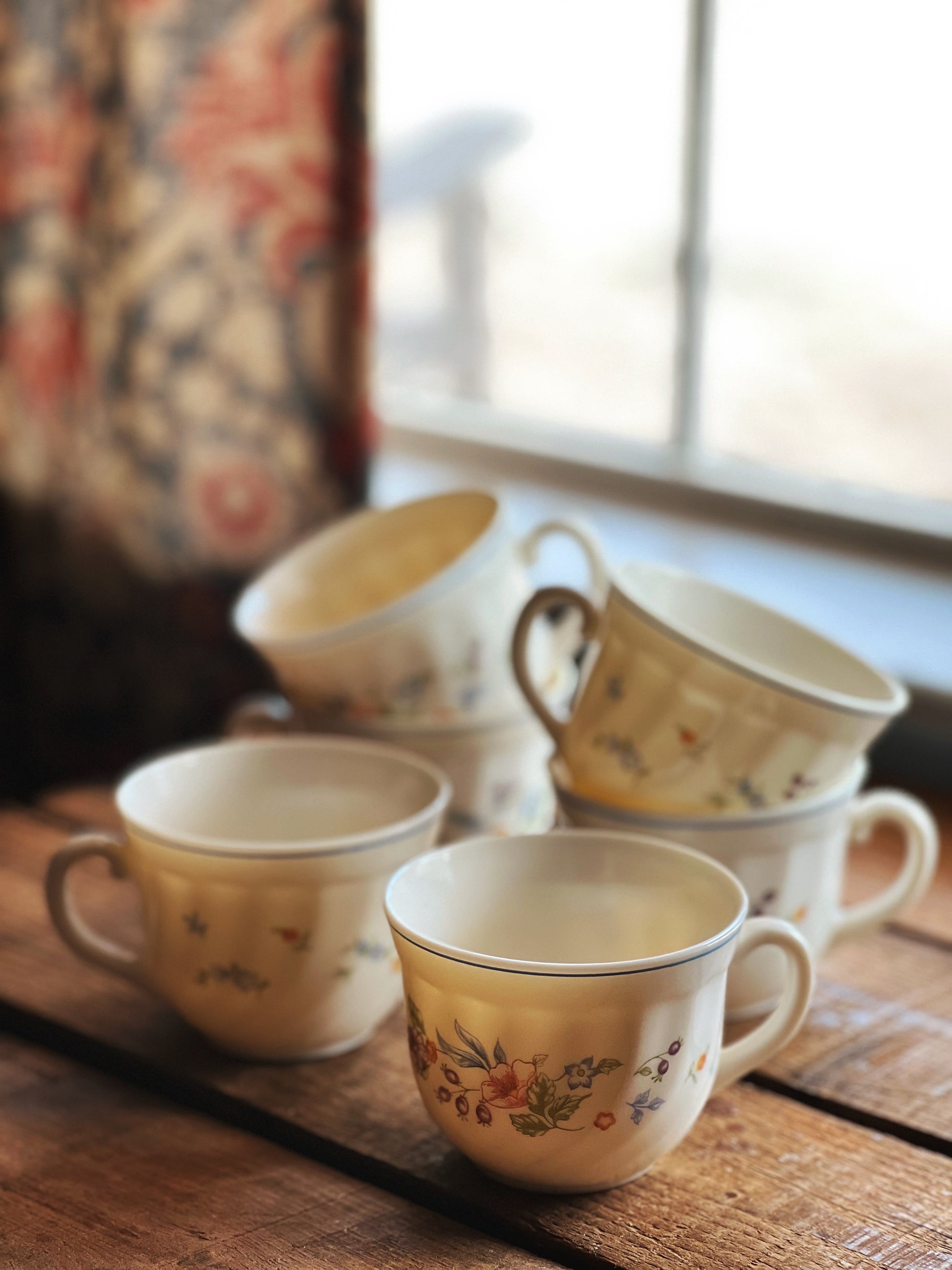 Set of vintage ceramic cups with floral patterns on a wooden surface.