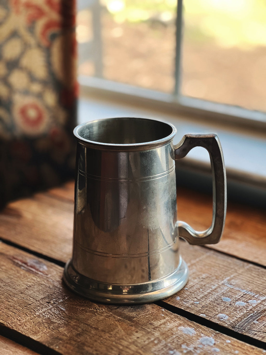 Silver tankard on a wooden surface with a window in the background