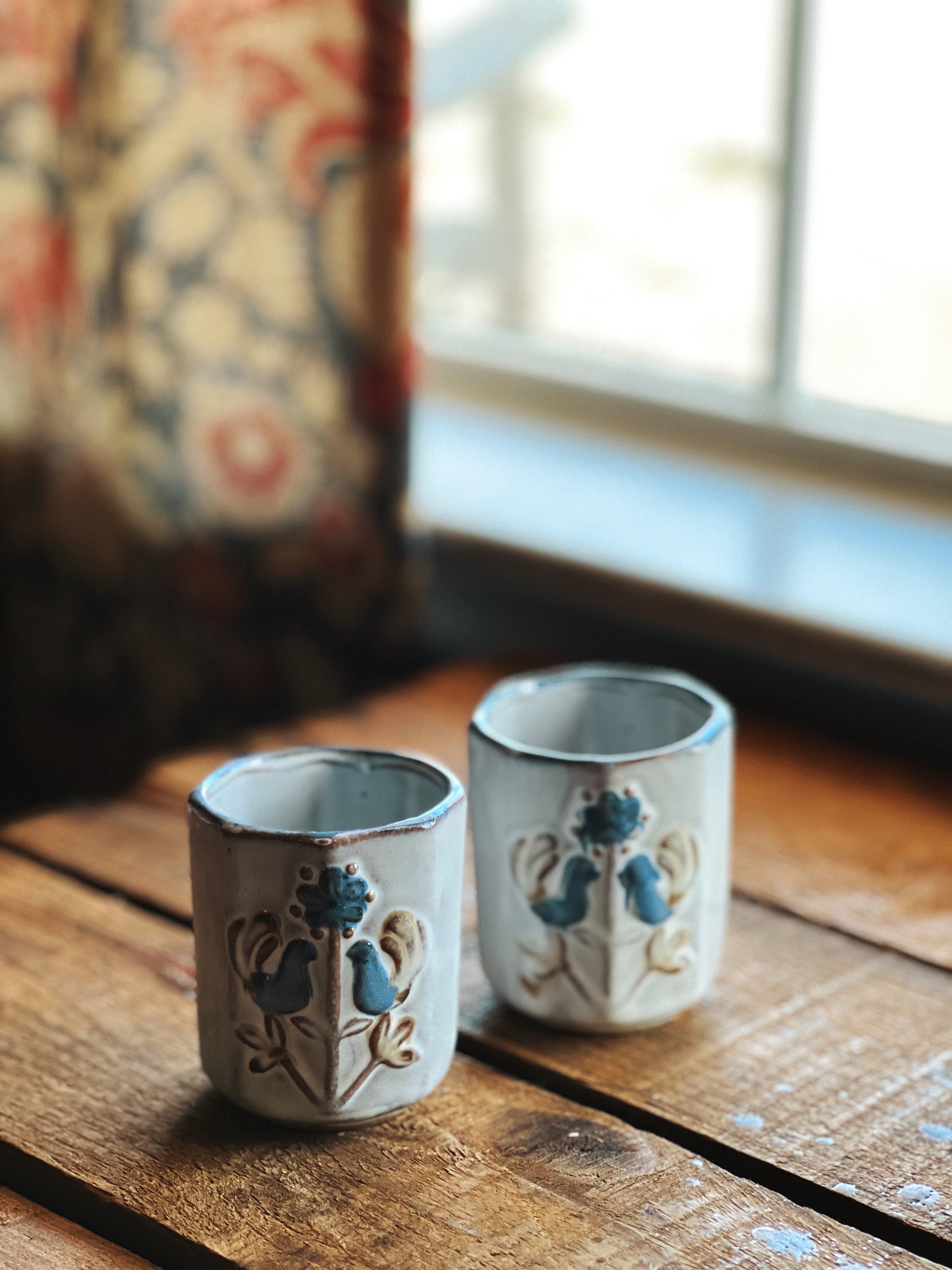 Two ceramic shot glasses with decorative designs on a wooden surface.