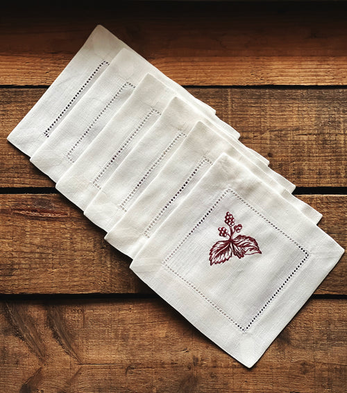 Set of white linen napkins with red embroidery on a wooden surface