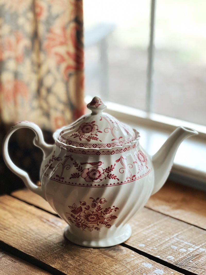 Vintage-style teapot with floral patterns on a wooden surface near a window.