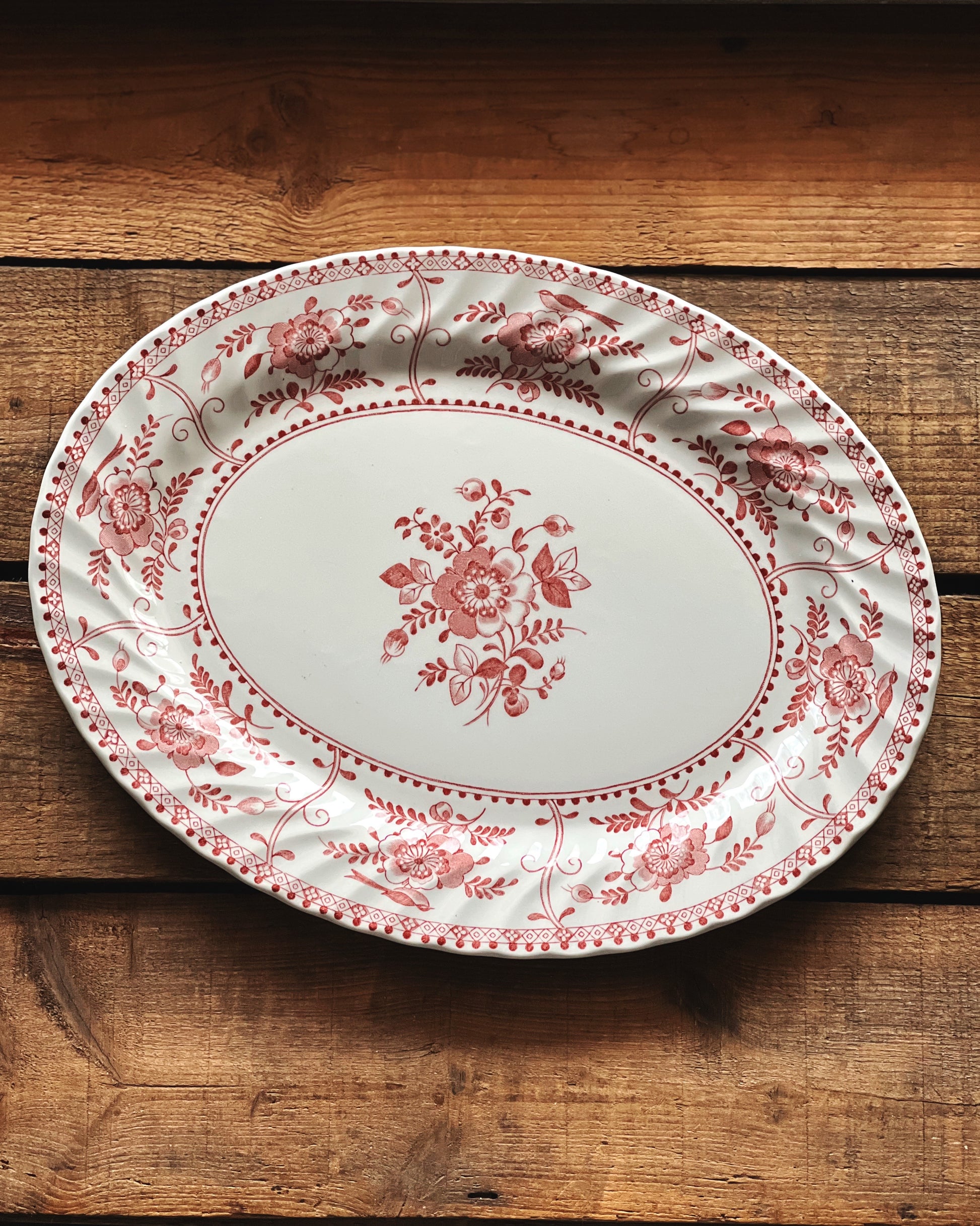 Decorative oval plate with red floral pattern on a wooden surface