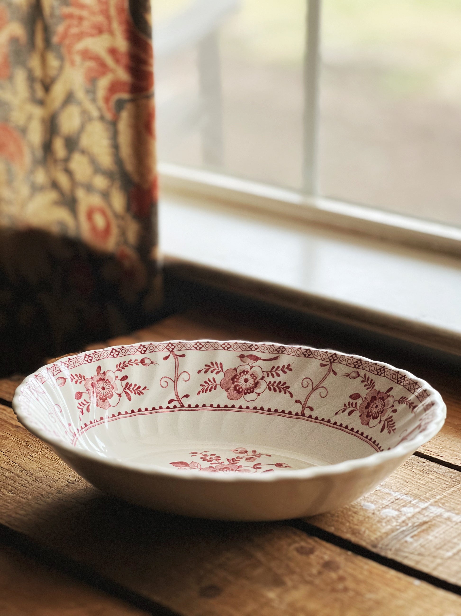 Decorative ceramic bowl with floral patterns on a wooden surface near a window.