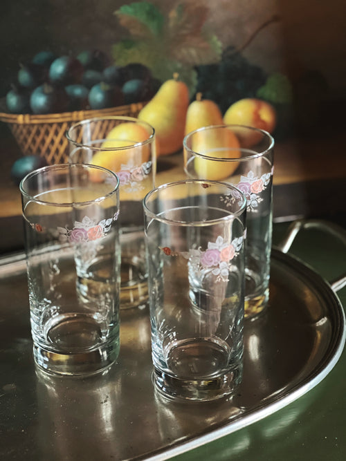 Four floral-decorated glasses on a metal tray with fruit in the background