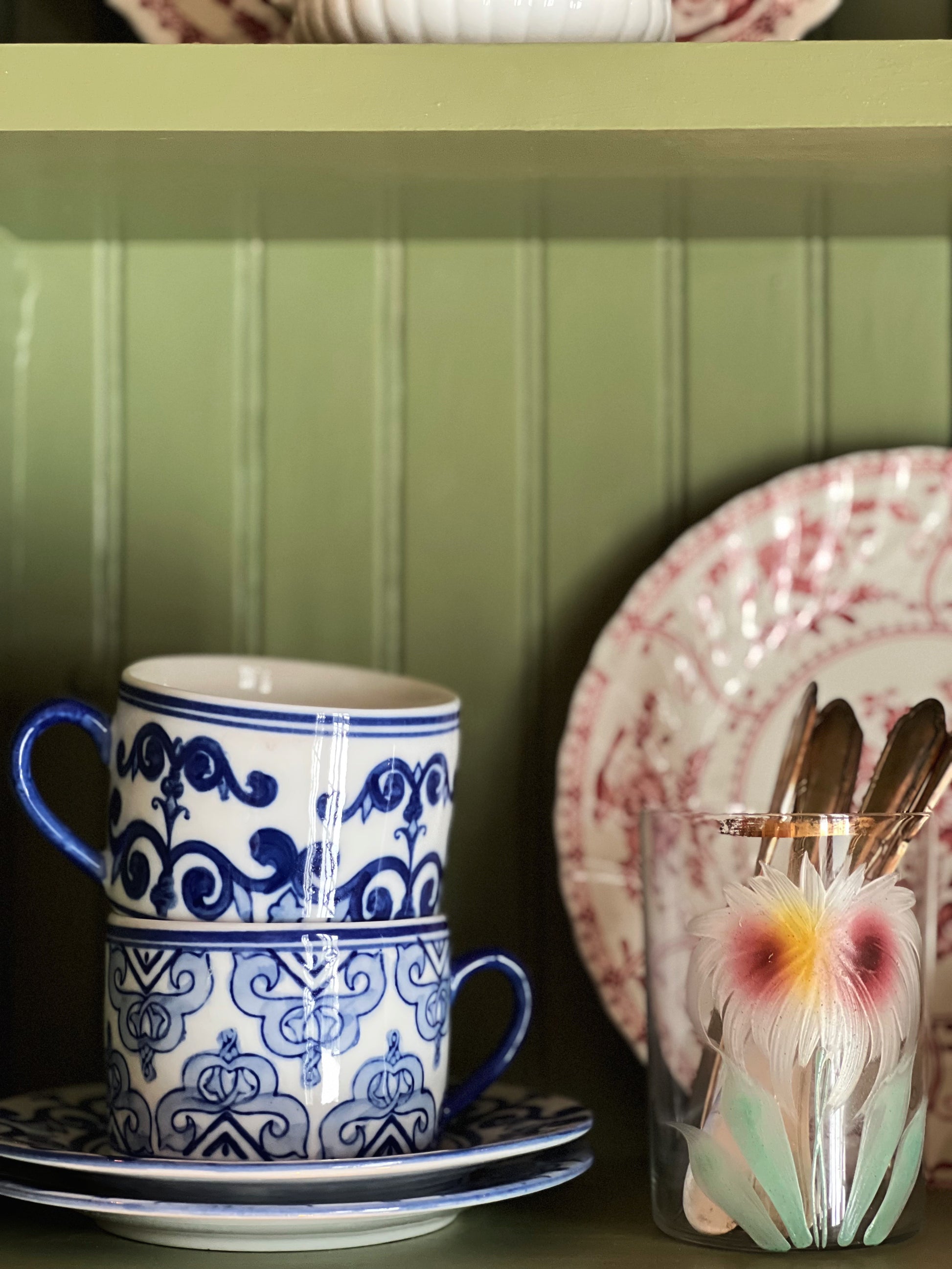 Ceramic mug with blue and white design on a green shelf with decorative plates and cutlery.