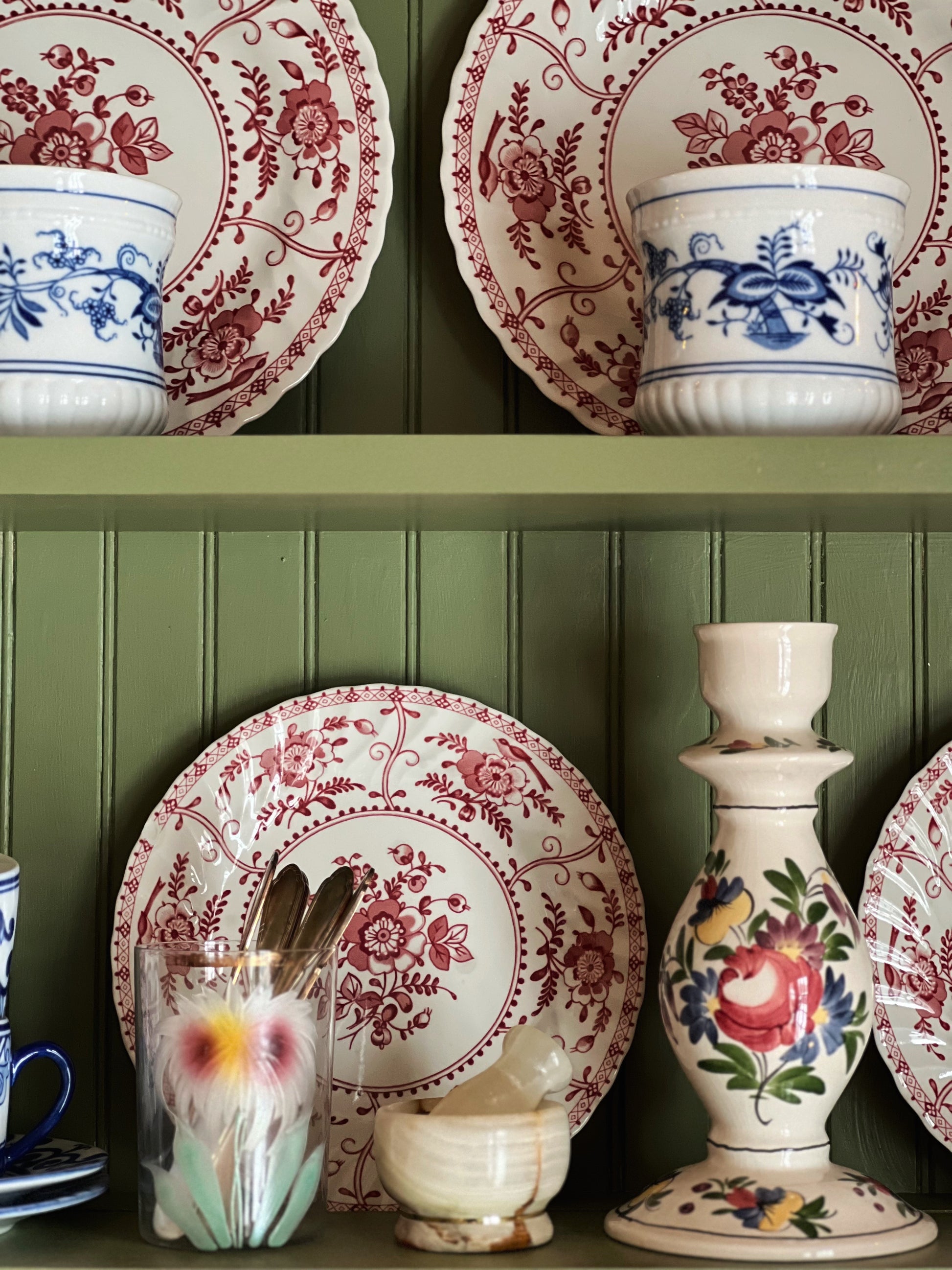 Decorative ceramic plates and vases with floral patterns on a green wooden shelf.