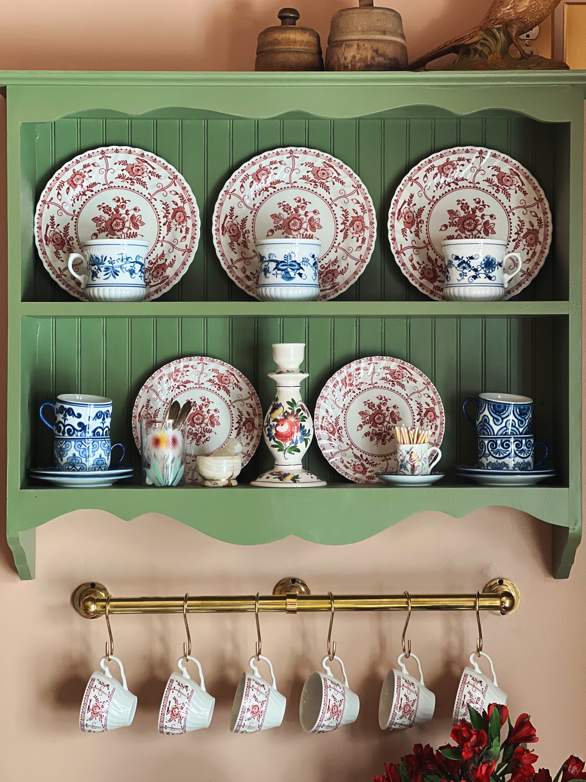 Vintage ceramic plates and cups displayed on a green shelf with a decorative gold rod below.