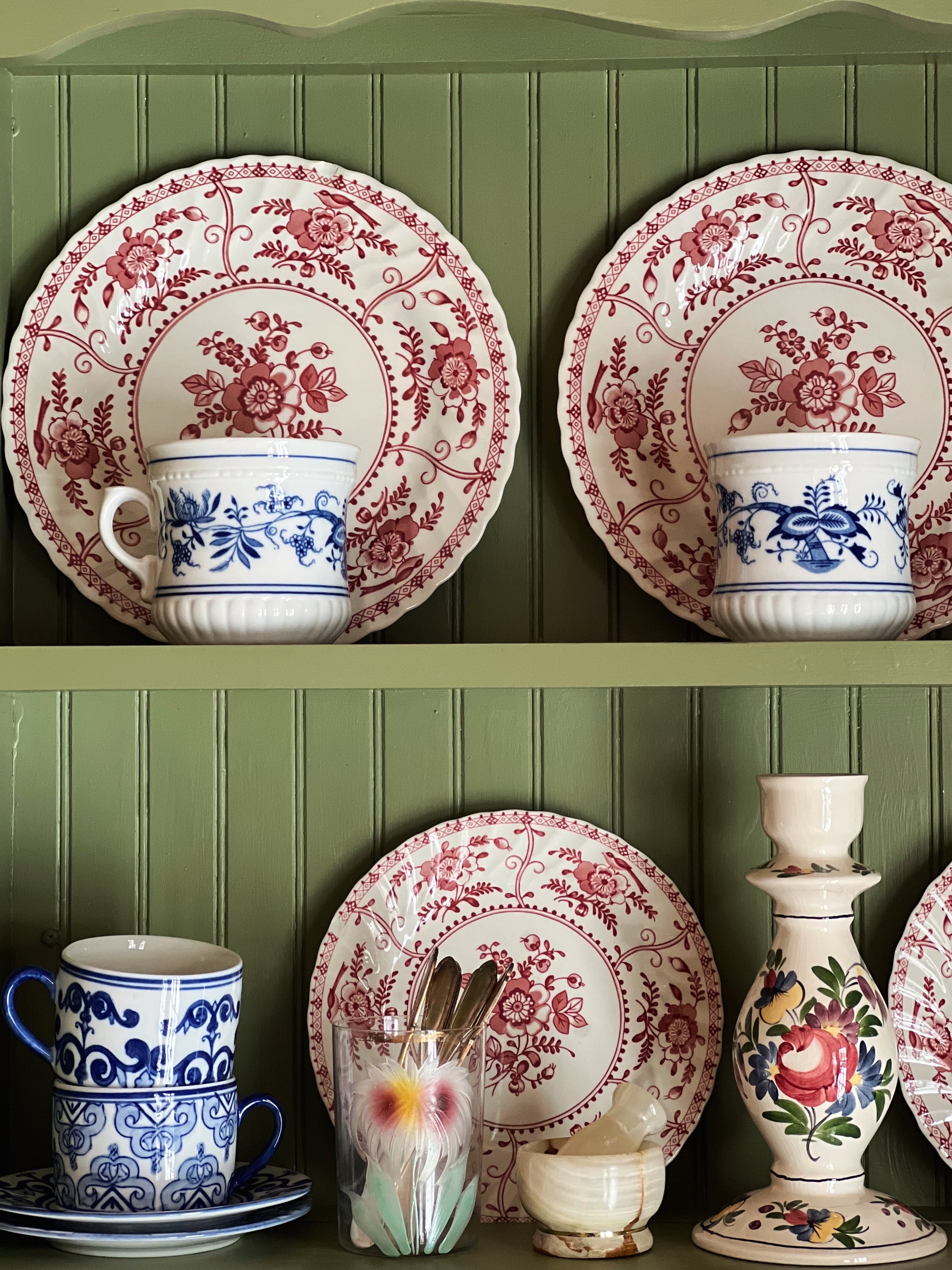 Decorative ceramic plates and cups with floral patterns on a green paneled wall.