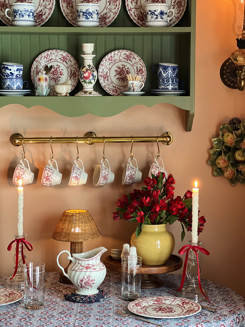 Vintage-style room with floral china, hanging teacups, and decorative items on a shelf.