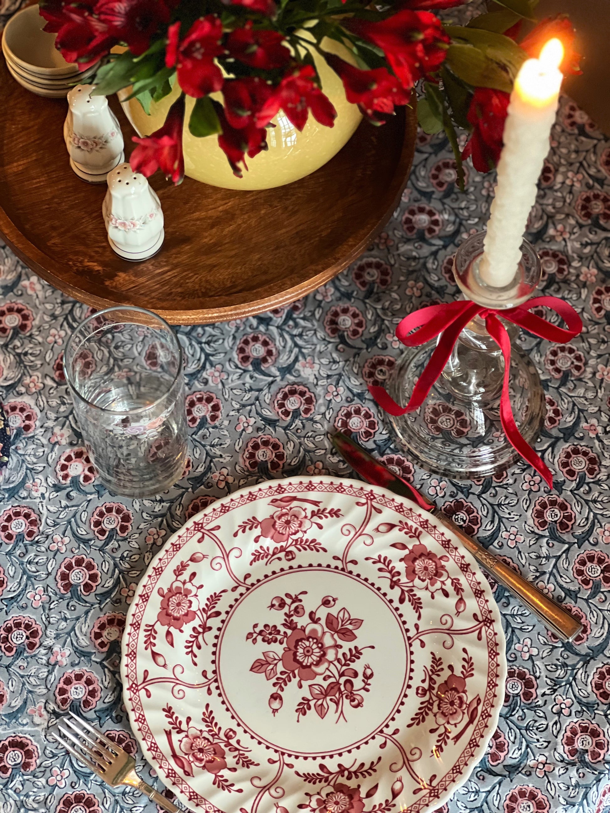 Decorative table setting with floral plates, candles, and cutlery on a patterned tablecloth.
