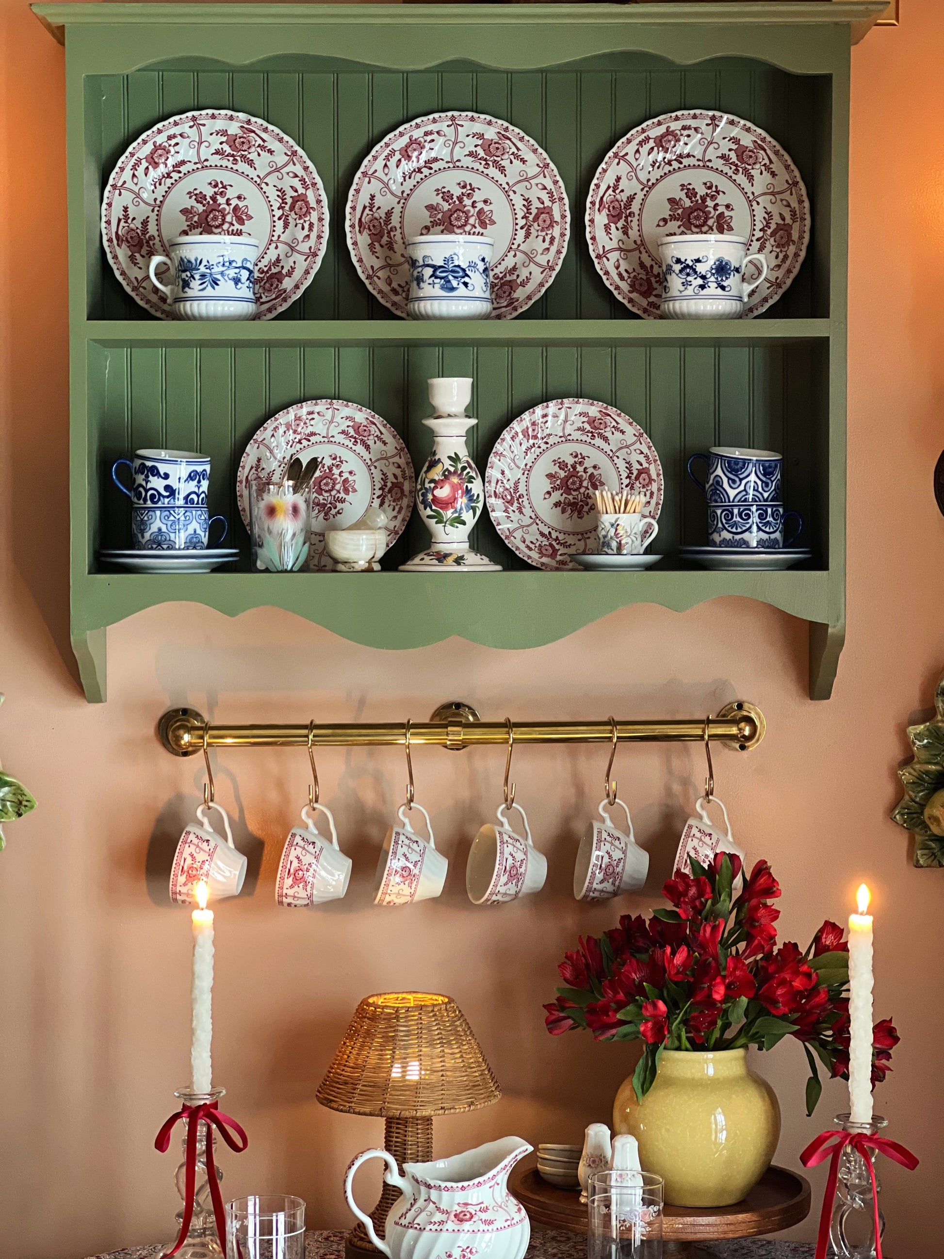 Decorative shelf with floral plates, hanging teacups, and a vase of red flowers.