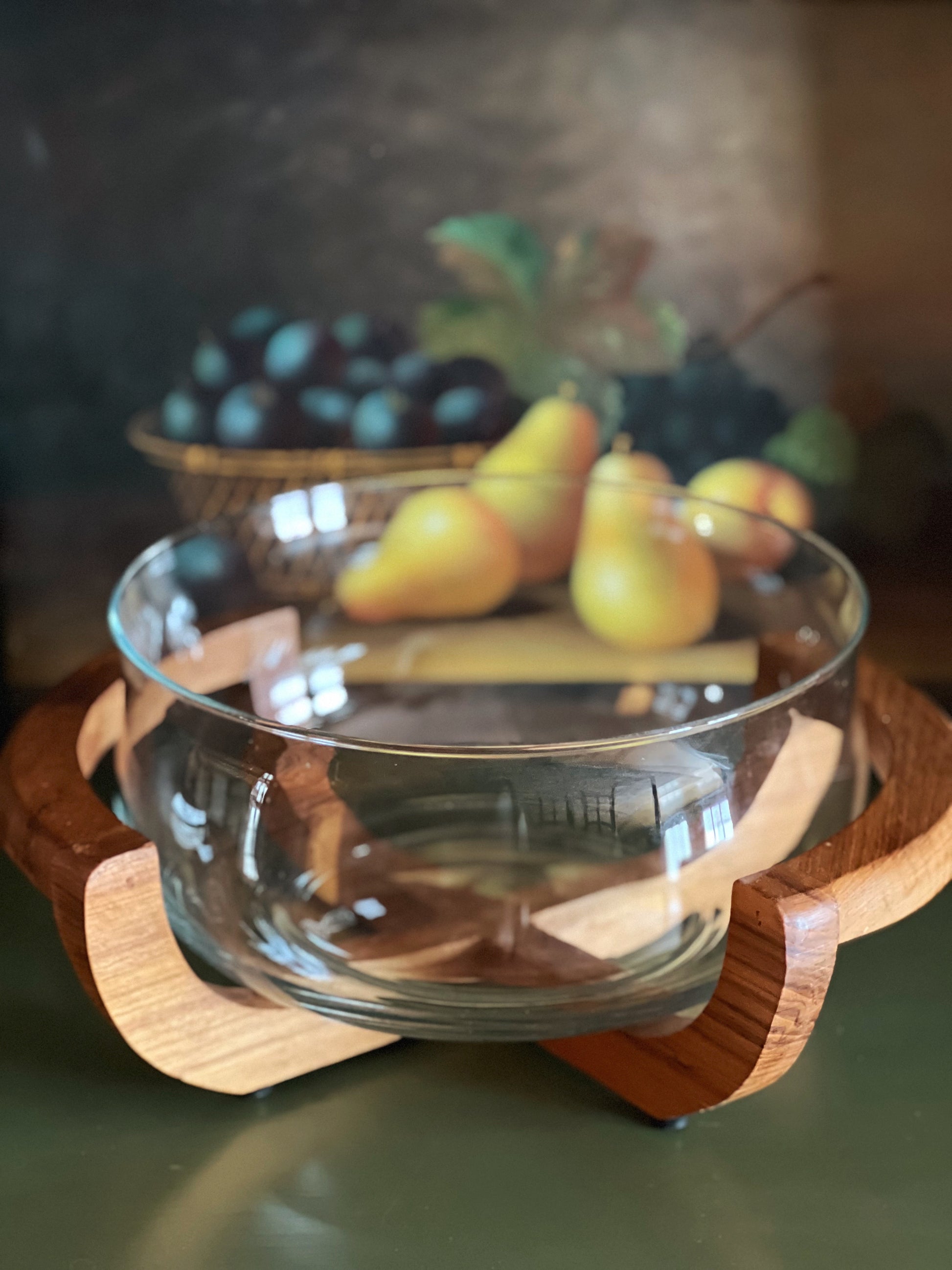 Clear glass bowl with wooden handle on a dark surface, containing pears and grapes.