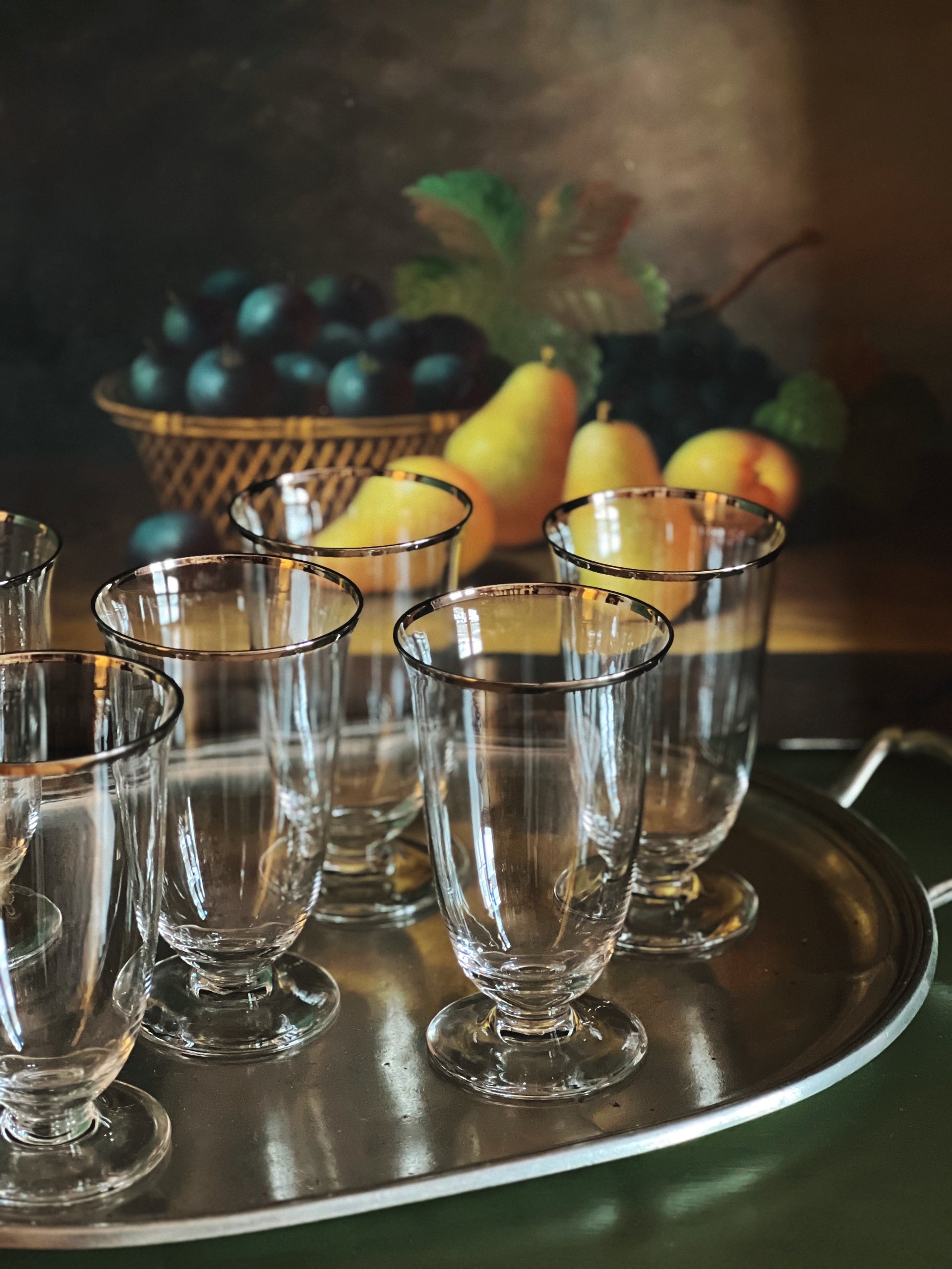 Set of clear glass dessert plates on a metal tray with fruit in the background