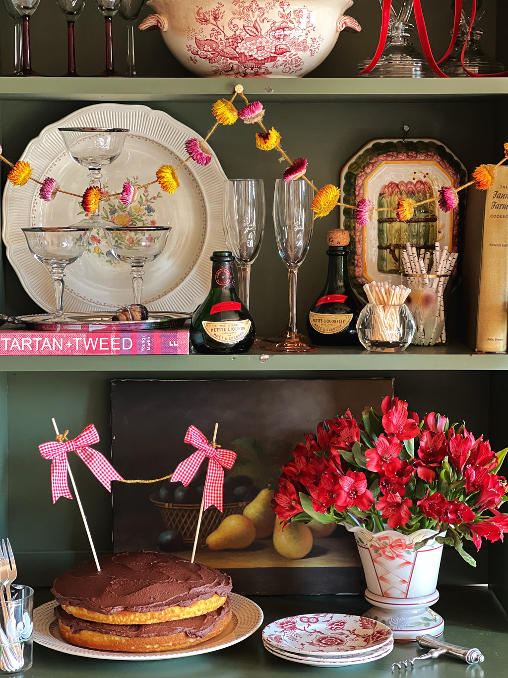 Decorative setting with plates, glasses, flowers, and a cake on a shelf.