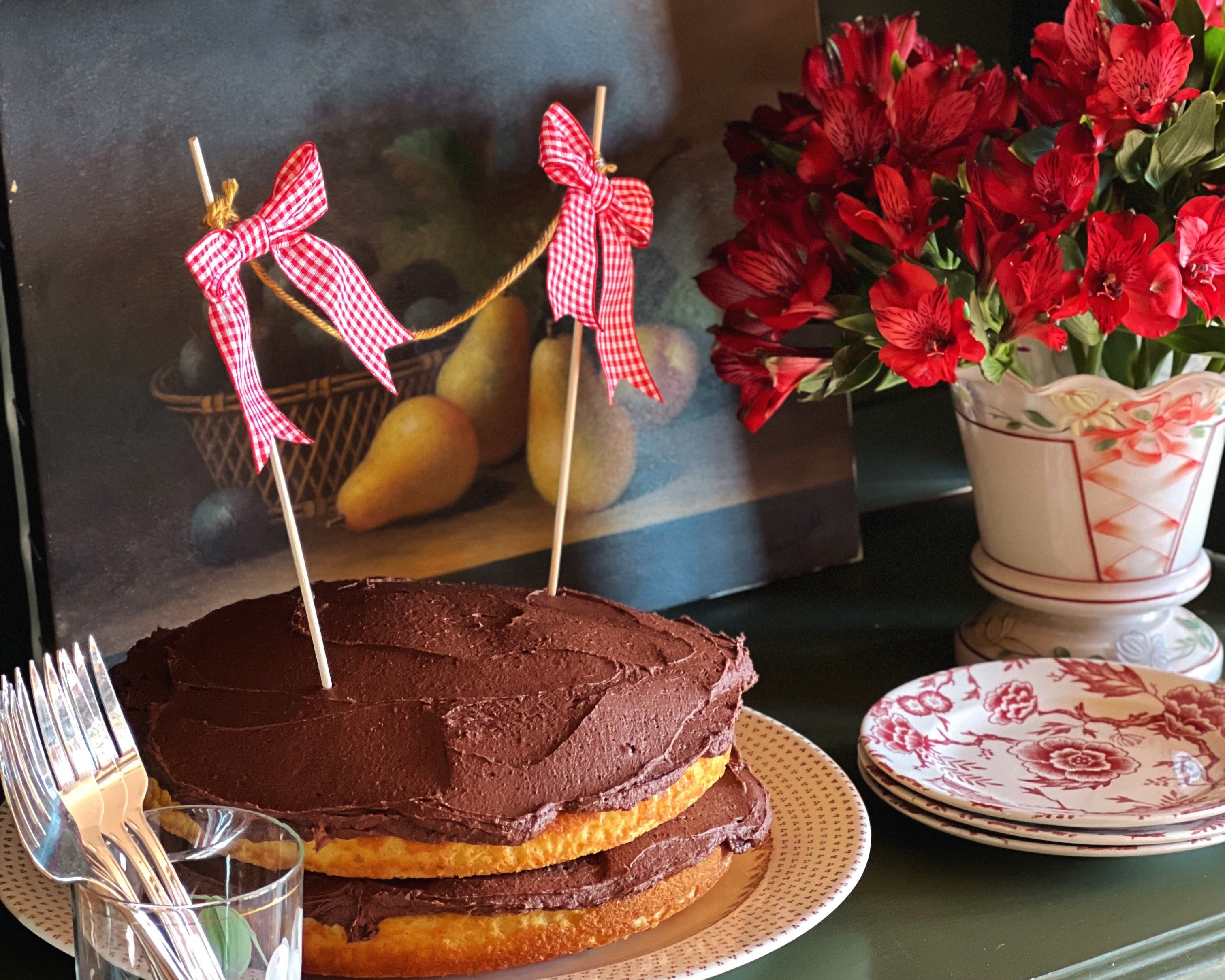 Chocolate cake with red ribbons on a table with flowers and books in the background